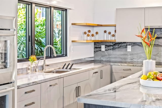 kitchen with white cabinetry, sink, and light stone countertops