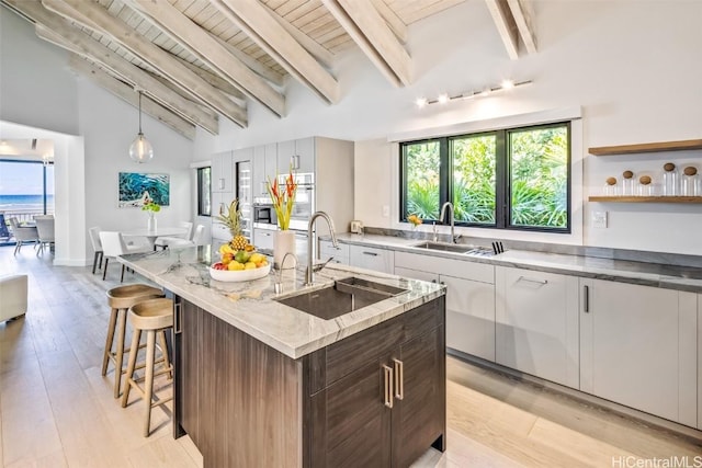 kitchen with sink, pendant lighting, a center island with sink, vaulted ceiling with beams, and white cabinetry