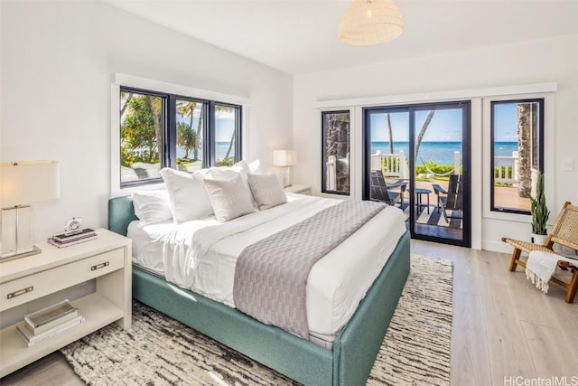 bedroom with a water view, light wood-type flooring, access to outside, and multiple windows