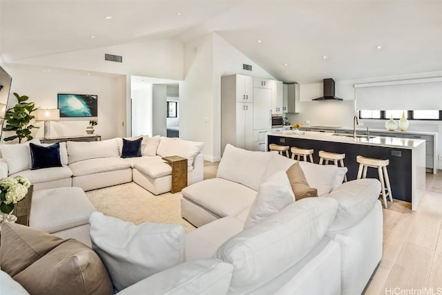 living room with sink, light hardwood / wood-style floors, and lofted ceiling