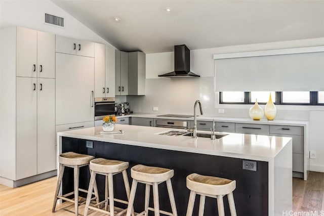 kitchen with sink, wall chimney range hood, vaulted ceiling, a kitchen bar, and a center island with sink