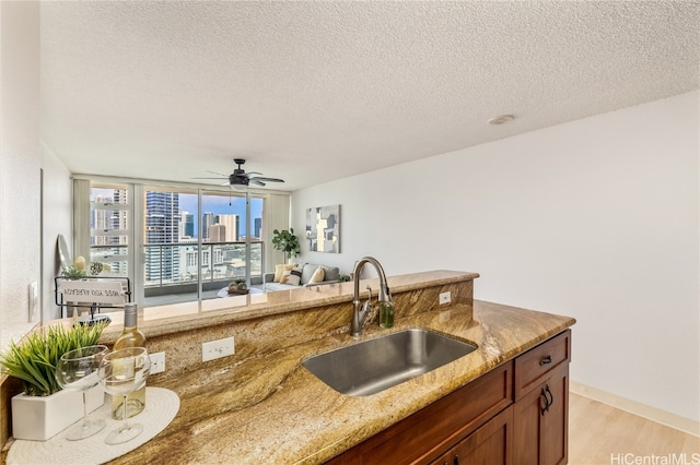 kitchen featuring light stone countertops, sink, light wood-type flooring, a textured ceiling, and ceiling fan