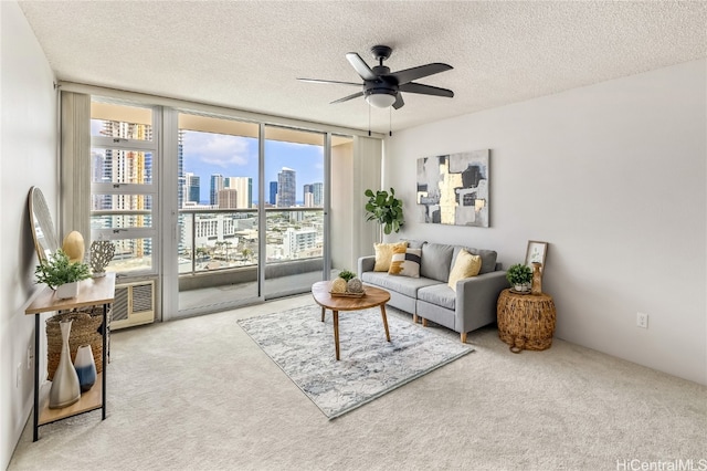 living room with ceiling fan, a textured ceiling, a wall of windows, and light colored carpet