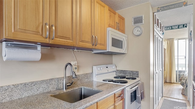 kitchen with a textured ceiling, light stone countertops, wood-type flooring, sink, and white appliances