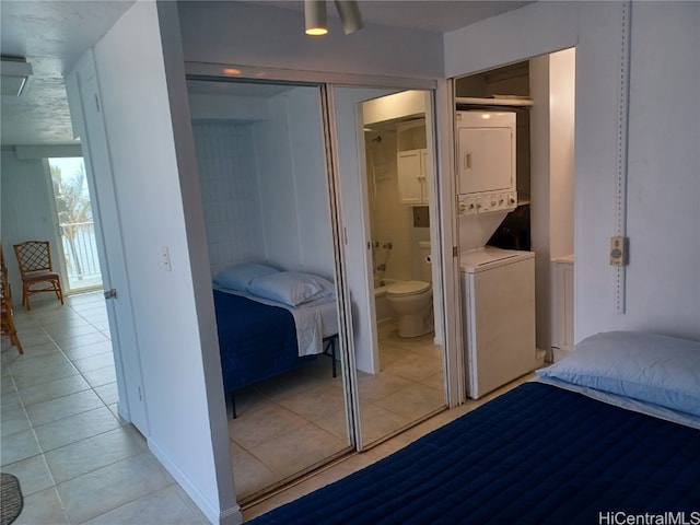 bedroom with light tile patterned flooring, a closet, ensuite bathroom, and stacked washer / dryer