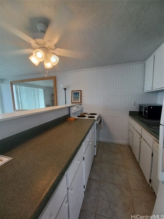 kitchen with white cabinets, ceiling fan, white electric range oven, tile walls, and dark tile patterned flooring