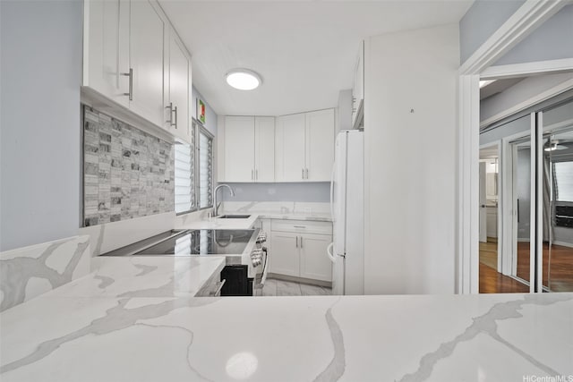 kitchen with light stone counters, a sink, stainless steel electric range, white cabinetry, and freestanding refrigerator