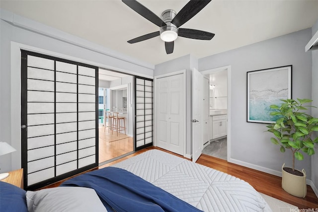 bedroom featuring wood finished floors, ensuite bathroom, a closet, ceiling fan, and baseboards