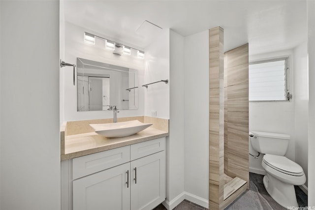 bathroom featuring a tile shower, toilet, vanity, and baseboards