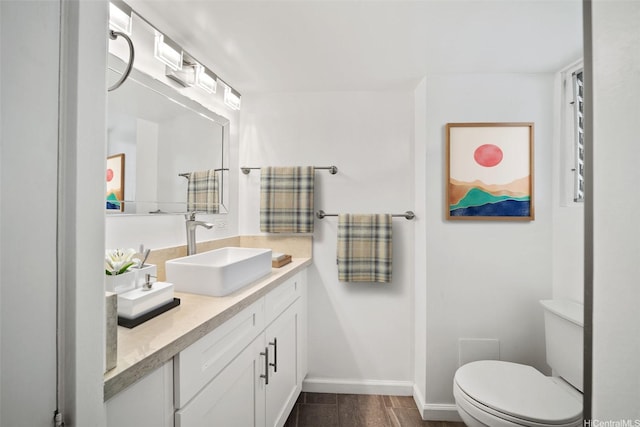 bathroom with wood finished floors, baseboards, vanity, and toilet