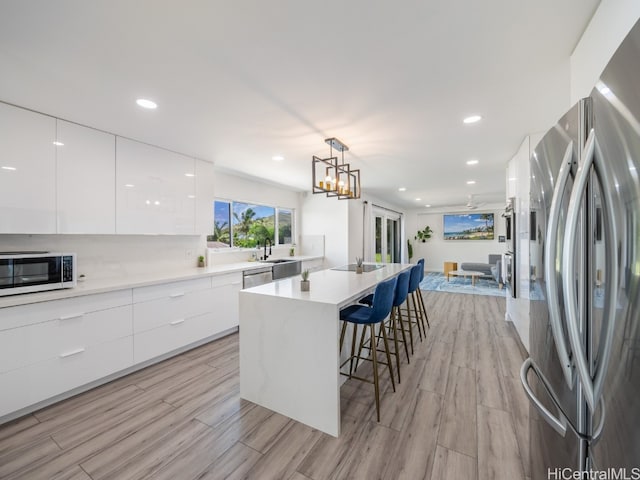 kitchen with light hardwood / wood-style floors, white cabinets, stainless steel appliances, and hanging light fixtures