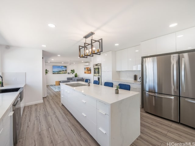 kitchen featuring appliances with stainless steel finishes, white cabinetry, pendant lighting, light hardwood / wood-style floors, and a center island