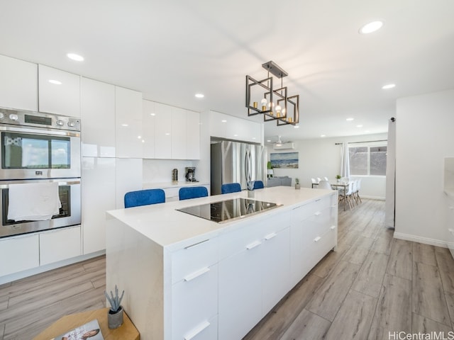 kitchen featuring light wood-type flooring, a kitchen island, white cabinetry, stainless steel appliances, and decorative light fixtures