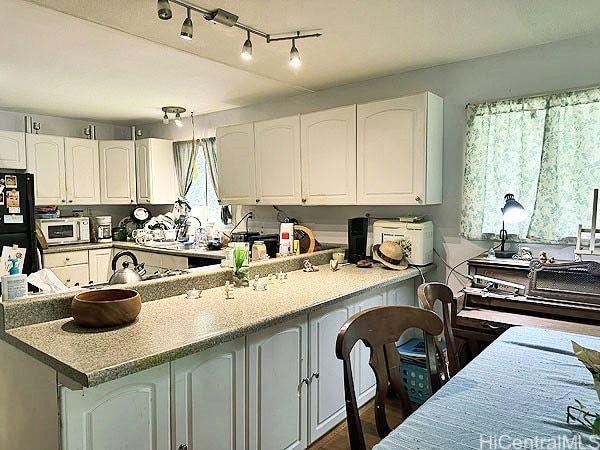 kitchen featuring white cabinetry, kitchen peninsula, and black refrigerator