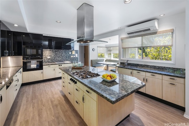 kitchen featuring a wall mounted air conditioner, a kitchen island, island range hood, stainless steel gas cooktop, and light hardwood / wood-style flooring