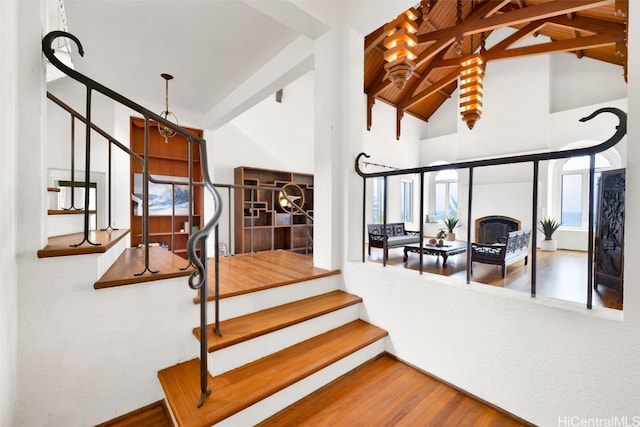 stairway featuring beam ceiling, wood-type flooring, and high vaulted ceiling