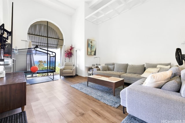 living room featuring beamed ceiling, a high ceiling, and light hardwood / wood-style floors