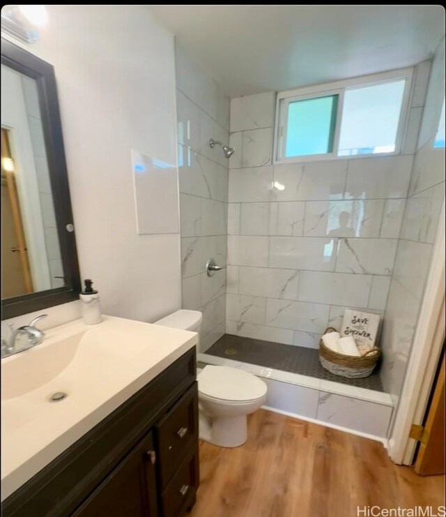 bathroom with wood-type flooring, toilet, vanity, and a tile shower