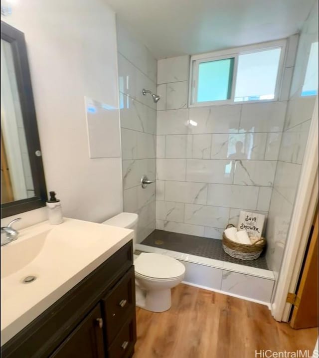 bathroom with hardwood / wood-style flooring, toilet, vanity, and a tile shower