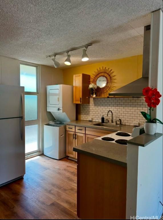 kitchen with fridge, sink, stacked washer and clothes dryer, backsplash, and dark hardwood / wood-style floors