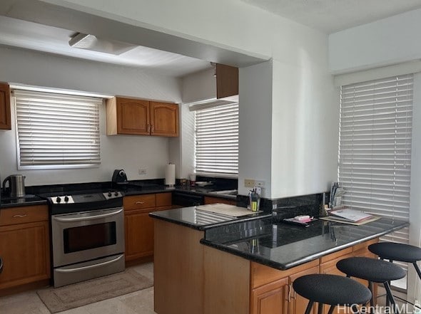 kitchen with stainless steel electric stove, dark stone counters, kitchen peninsula, and a kitchen breakfast bar