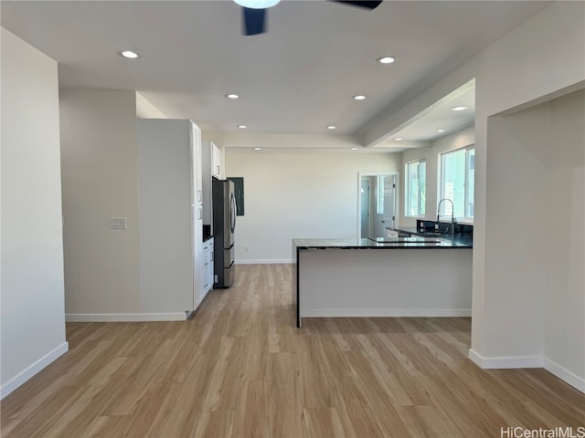 kitchen with sink, light wood-type flooring, kitchen peninsula, white cabinets, and stainless steel refrigerator