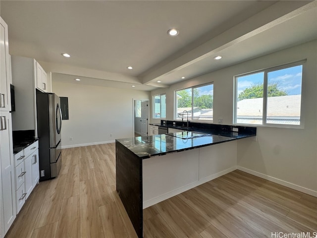 kitchen with kitchen peninsula, dark stone countertops, white cabinets, appliances with stainless steel finishes, and light hardwood / wood-style floors