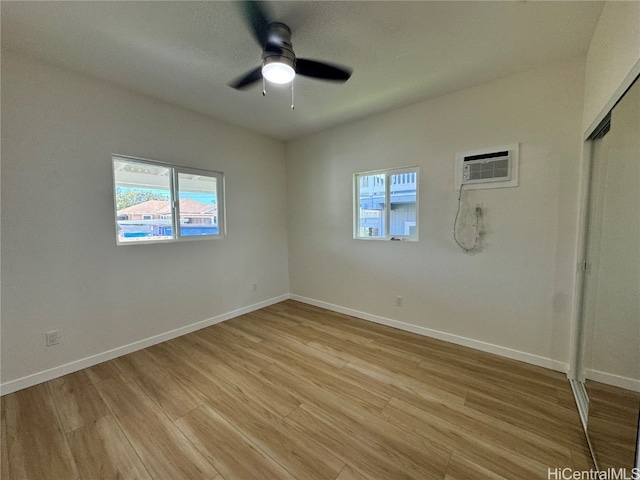 spare room featuring light hardwood / wood-style floors, ceiling fan, an AC wall unit, and a wealth of natural light