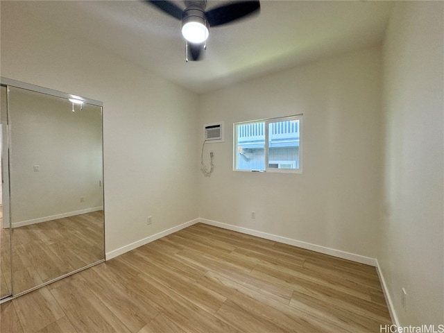 empty room featuring a wall mounted air conditioner, light wood-type flooring, and ceiling fan