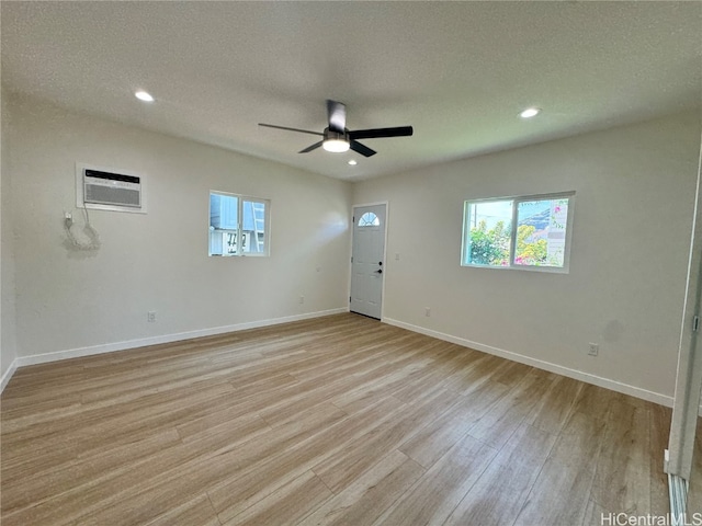 spare room with a wall unit AC, light hardwood / wood-style flooring, a textured ceiling, and ceiling fan