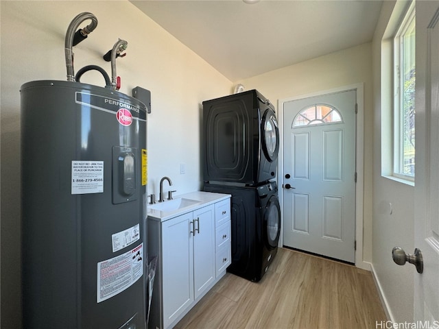 laundry room featuring stacked washer / drying machine, water heater, sink, light wood-type flooring, and cabinets