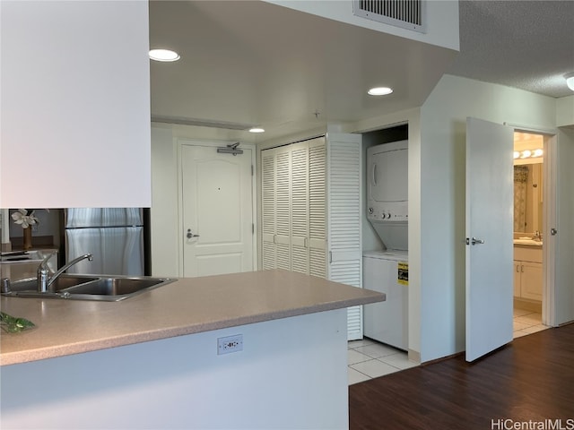 kitchen with stainless steel fridge, sink, stacked washer / dryer, and wood-type flooring