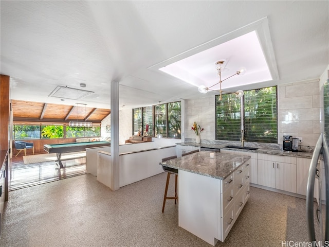 kitchen with a kitchen breakfast bar, a center island, white cabinetry, and tile walls