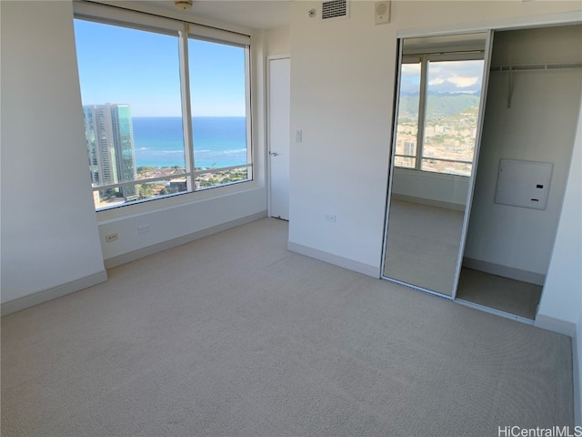 unfurnished bedroom featuring multiple windows, a closet, light colored carpet, and a water view