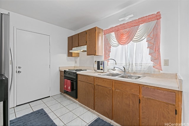 kitchen featuring light tile patterned floors, stainless steel refrigerator, sink, and black stove