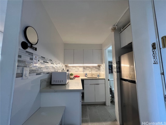 kitchen featuring sink, white cabinetry, backsplash, and stainless steel refrigerator