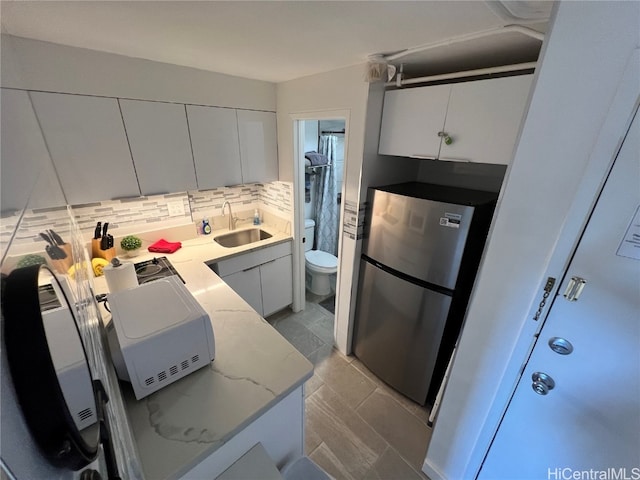 kitchen featuring tasteful backsplash, white cabinetry, stainless steel refrigerator, sink, and light stone counters