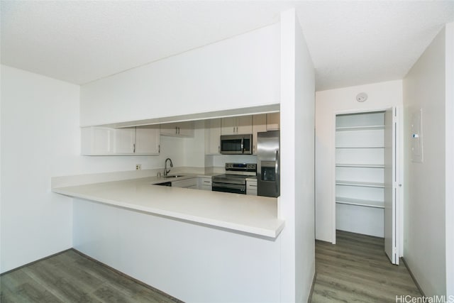 kitchen featuring kitchen peninsula, white cabinets, wood-type flooring, sink, and stainless steel appliances