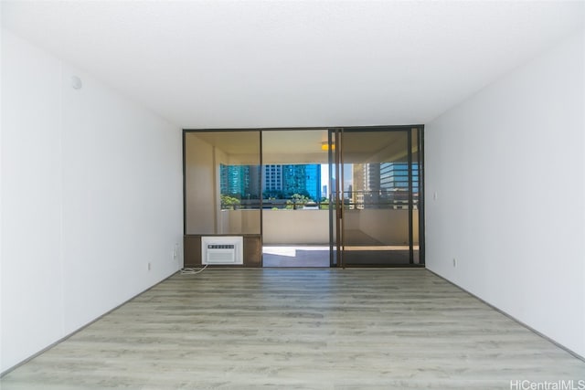 unfurnished room featuring an AC wall unit, expansive windows, and light hardwood / wood-style flooring