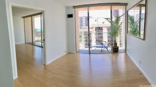 empty room with a wall of windows and light hardwood / wood-style floors