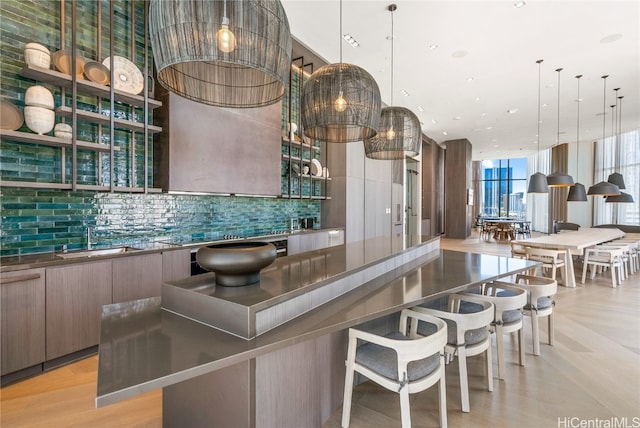 kitchen featuring decorative backsplash, hanging light fixtures, a spacious island, light hardwood / wood-style floors, and sink