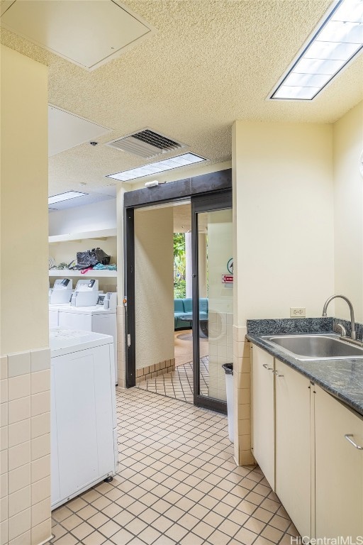 interior space with independent washer and dryer, sink, tile walls, white cabinets, and a textured ceiling