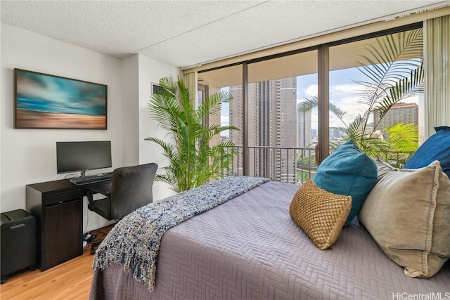 bedroom with access to exterior, expansive windows, a textured ceiling, and light hardwood / wood-style floors