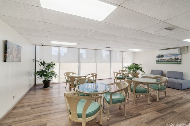 interior space featuring a wall unit AC, a wall of windows, a paneled ceiling, and wood-type flooring