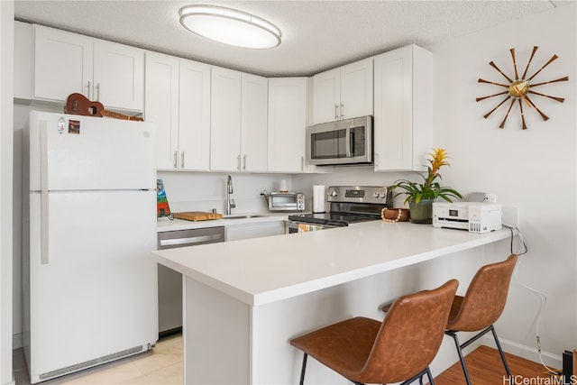 kitchen featuring sink, a textured ceiling, kitchen peninsula, white cabinetry, and stainless steel appliances