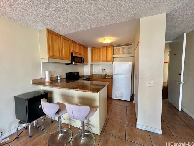 kitchen with black range oven, white refrigerator, kitchen peninsula, a textured ceiling, and a breakfast bar