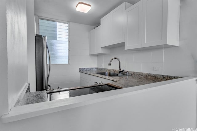 kitchen featuring white cabinetry, sink, light stone counters, and stainless steel refrigerator