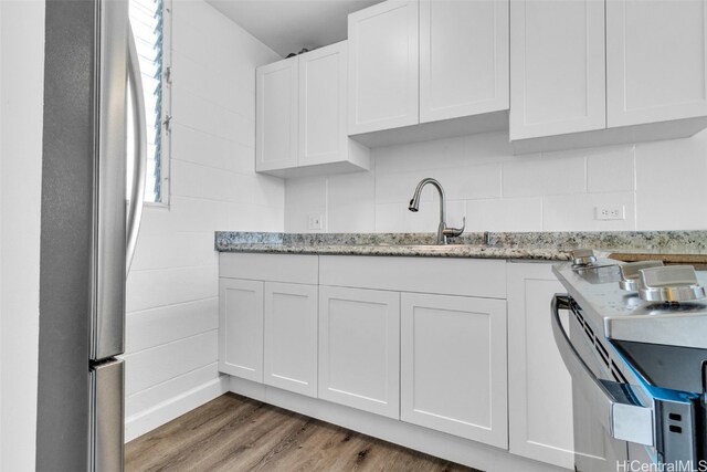 kitchen with stainless steel appliances, sink, light stone counters, hardwood / wood-style floors, and white cabinets