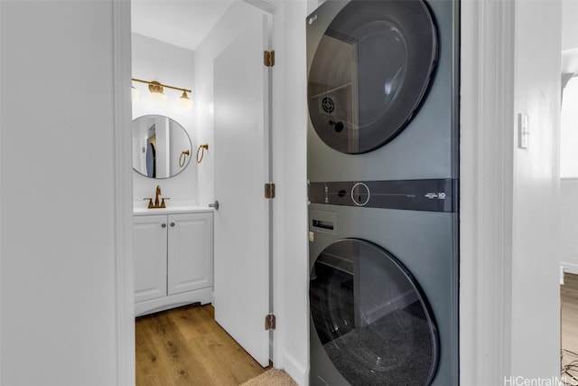 clothes washing area with stacked washer / drying machine, sink, and light hardwood / wood-style floors