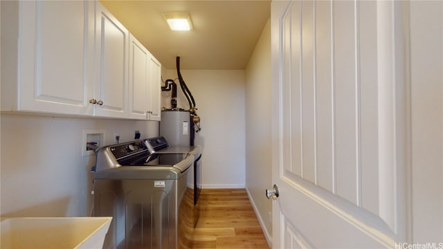 laundry area with cabinets, washing machine and clothes dryer, water heater, light hardwood / wood-style floors, and sink